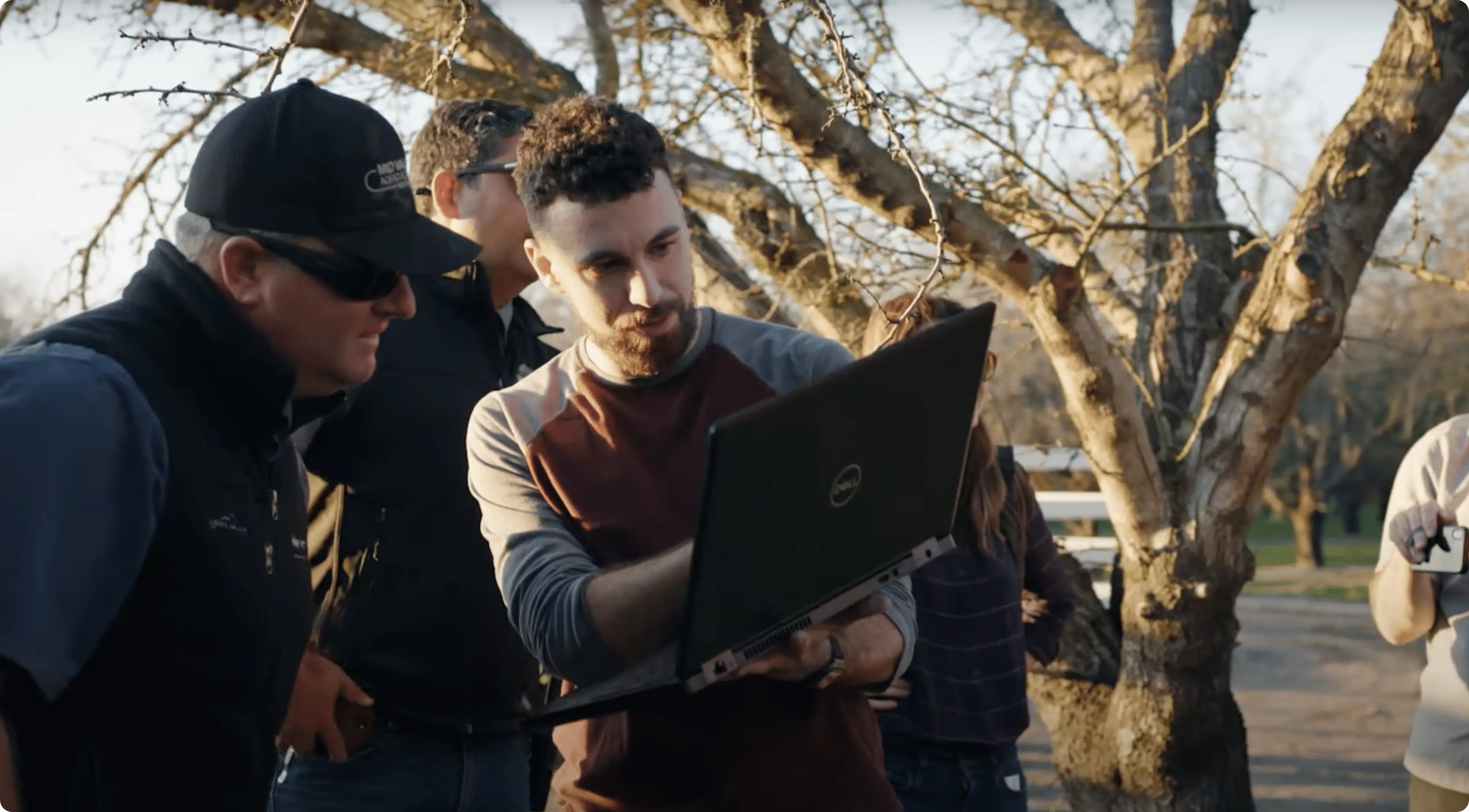 A man shows a computer to another man in a field