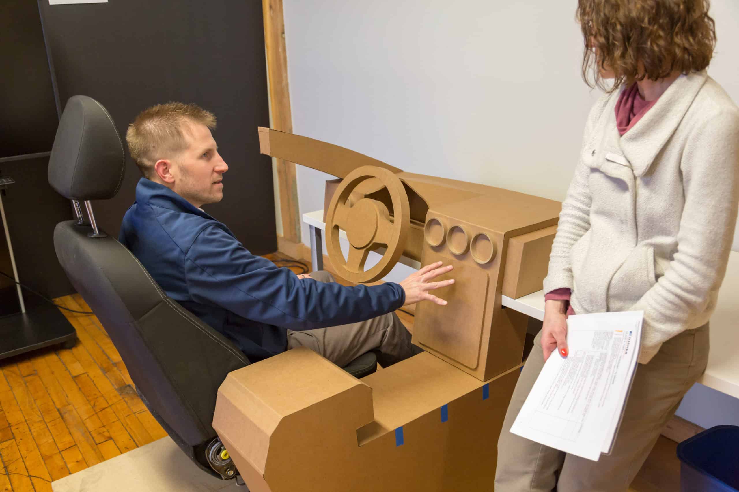 A man sitting at a cardboard prototype being interviewed
