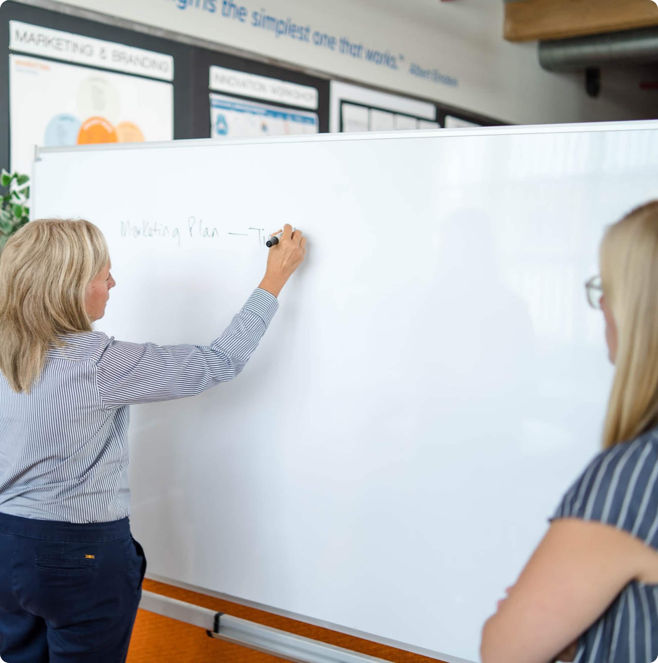 A women writes on a whiteboard while another woman watches