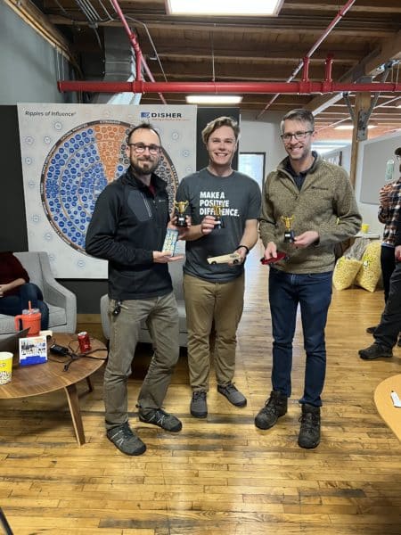 Three DISHER employees holding up their derby cars and awards