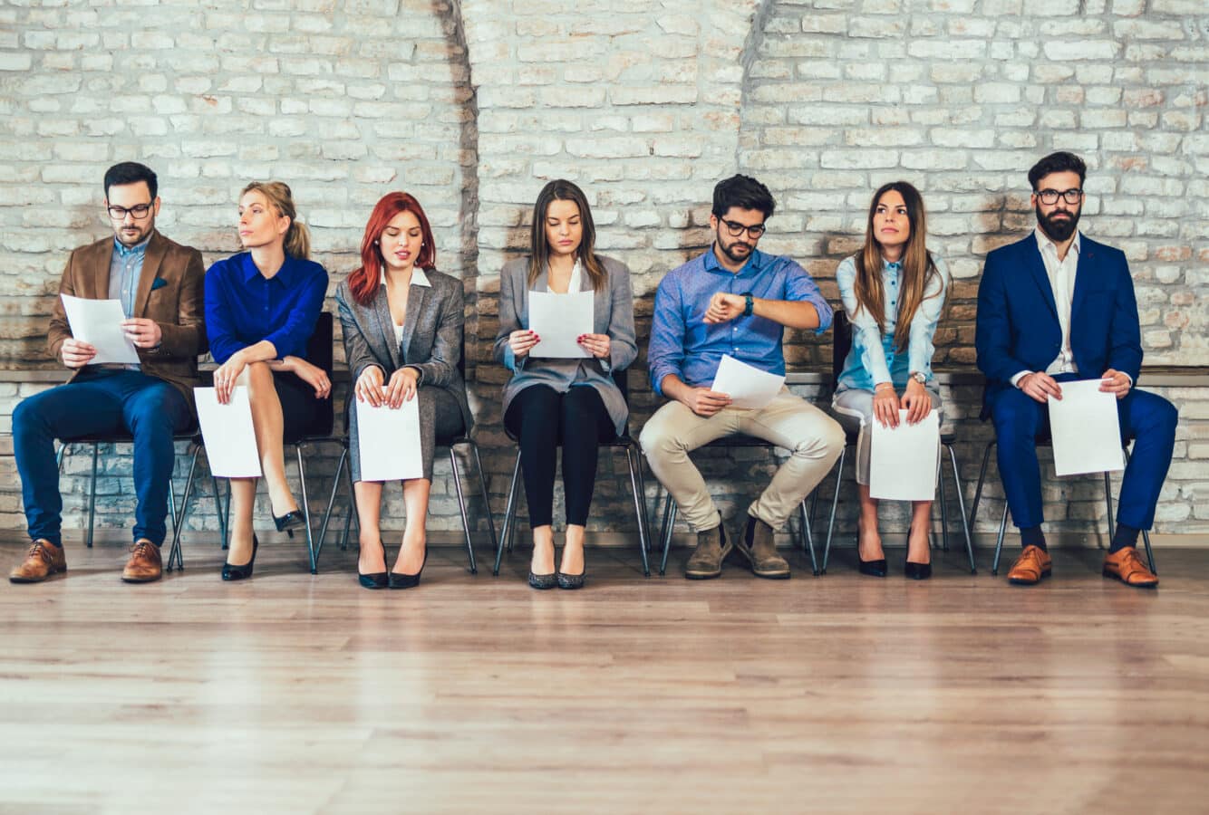 a row of people sitting in chairs waiting for a job interview