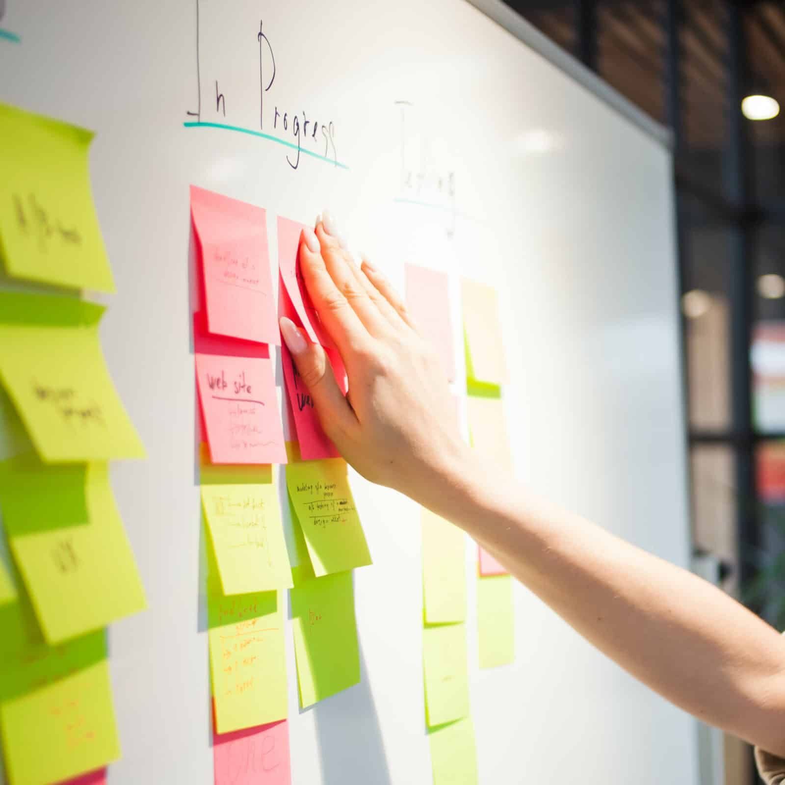 A person sticks a sticky note to an agile project management board