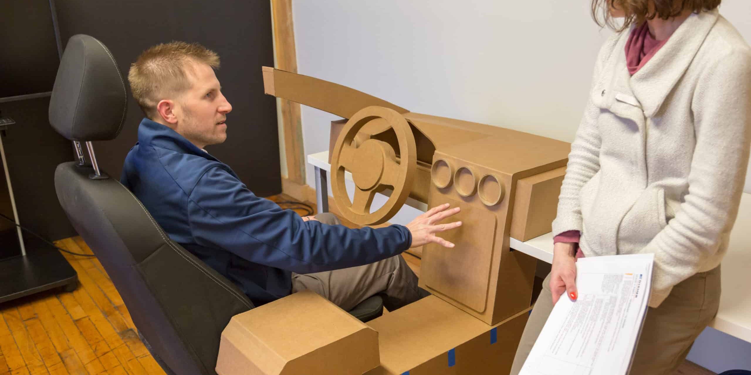 A man sitting at a cardboard prototype being interviewed