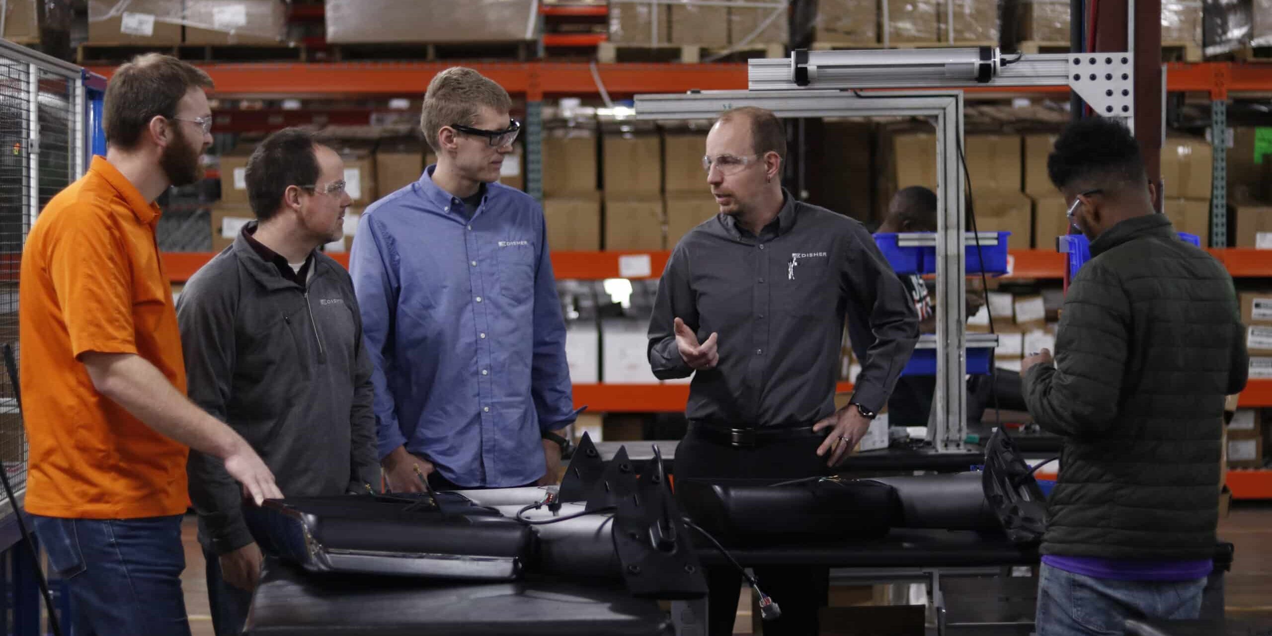 Four engineers stand in a manufacturing space discussing processes