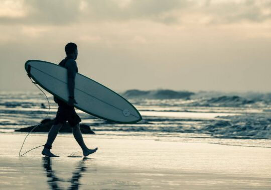 A surfer walking out into the water on a beach